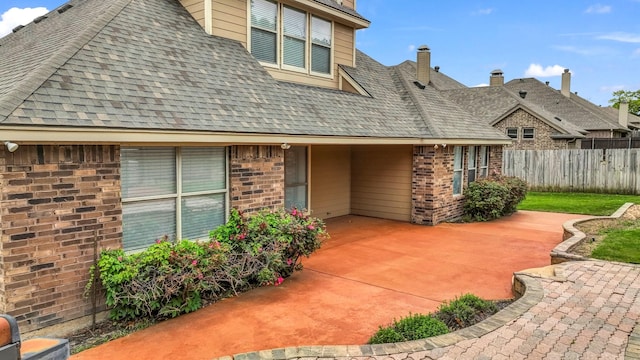 exterior space with brick siding, fence, a patio, and roof with shingles