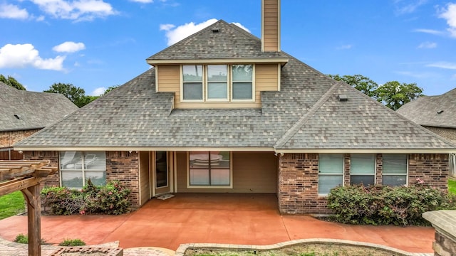 back of house with roof with shingles, a patio, a chimney, and brick siding