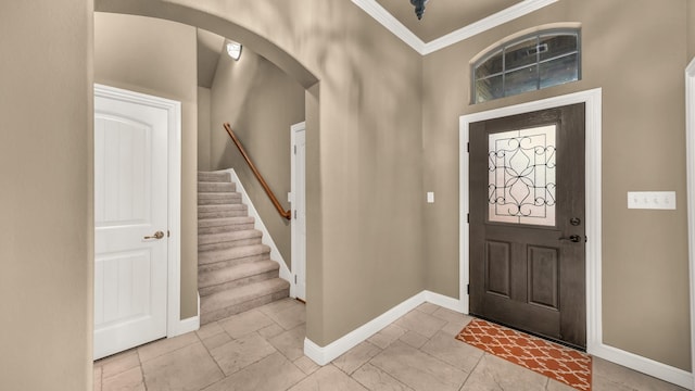 entryway with baseboards, arched walkways, crown molding, and stairway