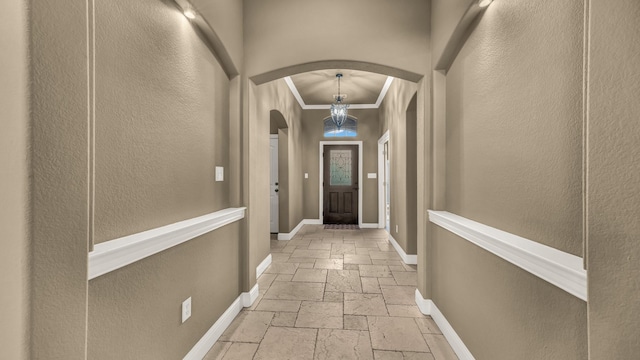 interior space with stone tile flooring, an inviting chandelier, ornamental molding, baseboards, and arched walkways