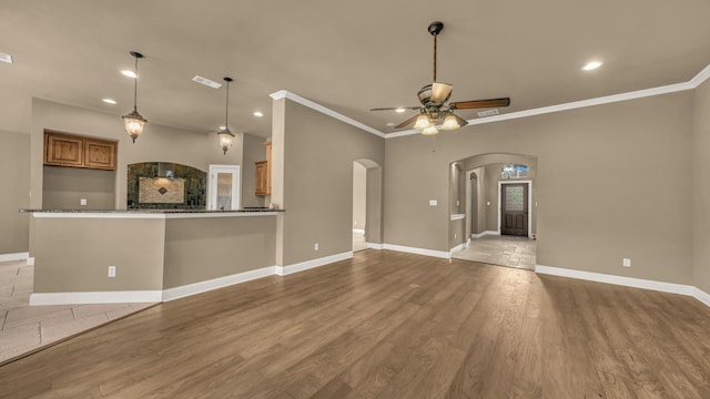 unfurnished living room with crown molding, arched walkways, baseboards, and a ceiling fan