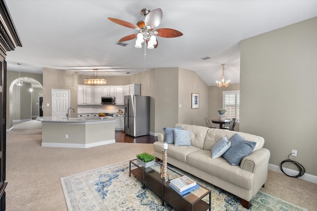 living area featuring arched walkways, dark carpet, ceiling fan with notable chandelier, baseboards, and visible vents