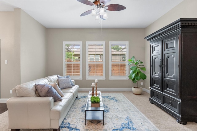 living area featuring baseboards, light carpet, and a ceiling fan
