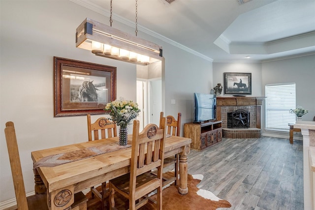 dining room featuring ornamental molding, a brick fireplace, wood finished floors, baseboards, and a tray ceiling