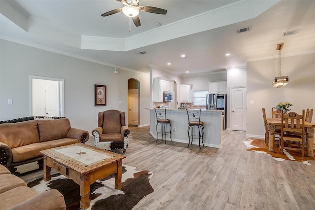 living area with visible vents, arched walkways, light wood-style flooring, and a ceiling fan
