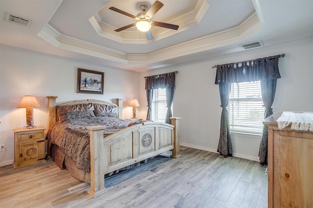 bedroom with a tray ceiling, visible vents, and light wood-style floors