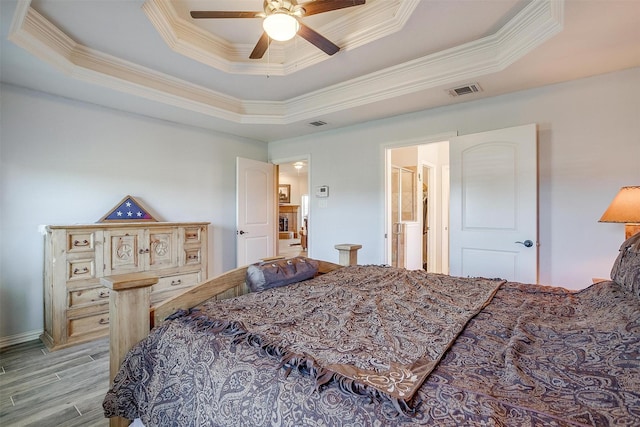 bedroom with crown molding, visible vents, wood finished floors, a tray ceiling, and a ceiling fan