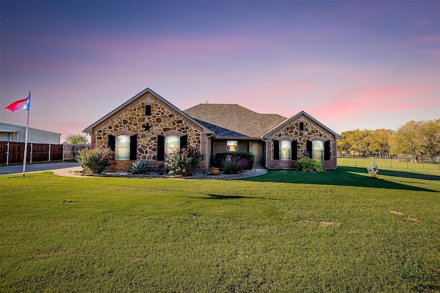 view of front facade featuring a lawn, brick siding, fence, and stone siding