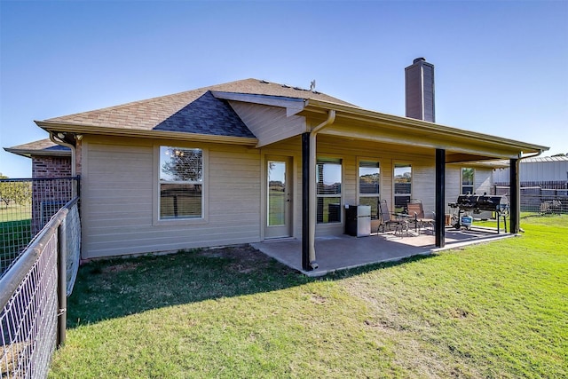 rear view of property featuring fence, a patio, roof with shingles, a chimney, and a lawn