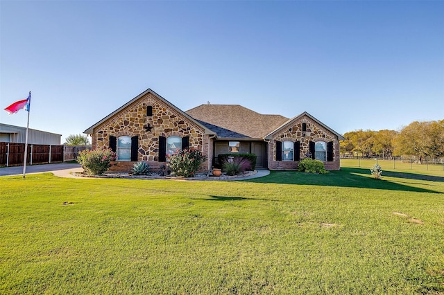 view of front of home featuring brick siding, stone siding, fence, and a front yard