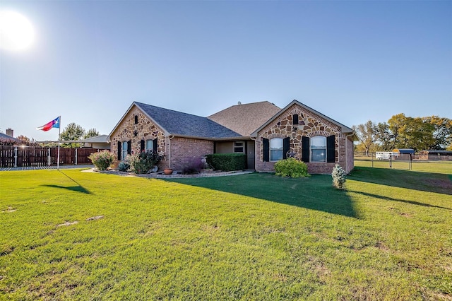 view of front facade with fence, roof with shingles, stone siding, brick siding, and a front yard