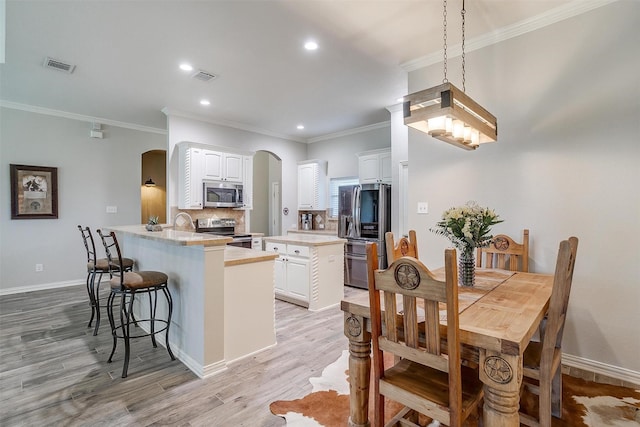kitchen featuring appliances with stainless steel finishes, arched walkways, white cabinetry, a peninsula, and visible vents
