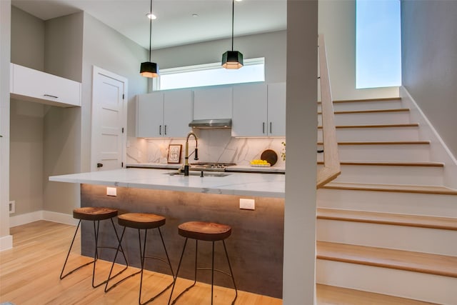 kitchen with light stone countertops, a sink, a kitchen breakfast bar, backsplash, and under cabinet range hood