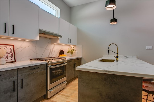kitchen with a peninsula, under cabinet range hood, light stone counters, a sink, and gas stove