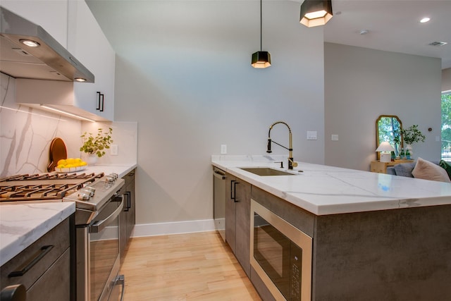 kitchen featuring wall chimney range hood, appliances with stainless steel finishes, a sink, a peninsula, and visible vents
