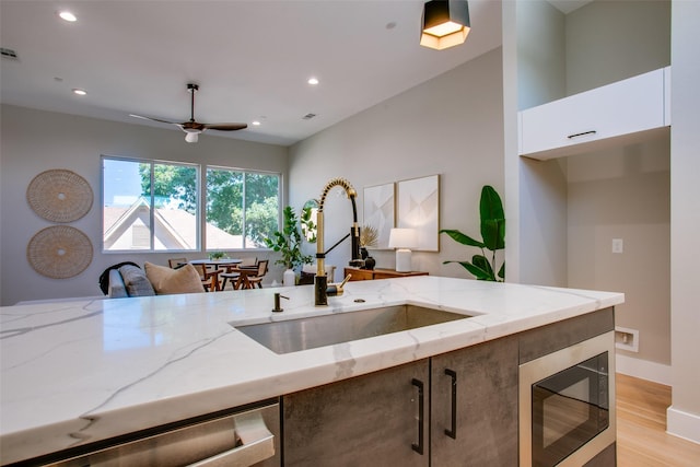 kitchen with light stone countertops, built in microwave, white cabinets, a sink, and light wood finished floors
