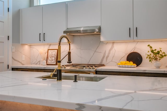 room details with under cabinet range hood, light stone counters, and tasteful backsplash