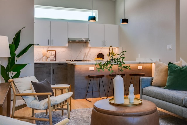 interior space featuring open floor plan, under cabinet range hood, tasteful backsplash, light wood finished floors, and decorative light fixtures