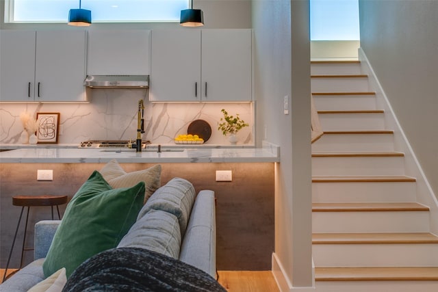 kitchen featuring decorative light fixtures, tasteful backsplash, a sink, light wood-style floors, and under cabinet range hood