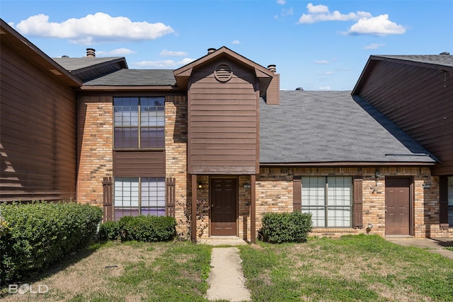 view of front of home featuring roof with shingles, a front lawn, and brick siding