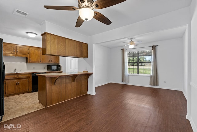 kitchen with dark wood-type flooring, a sink, brown cabinets, and black appliances