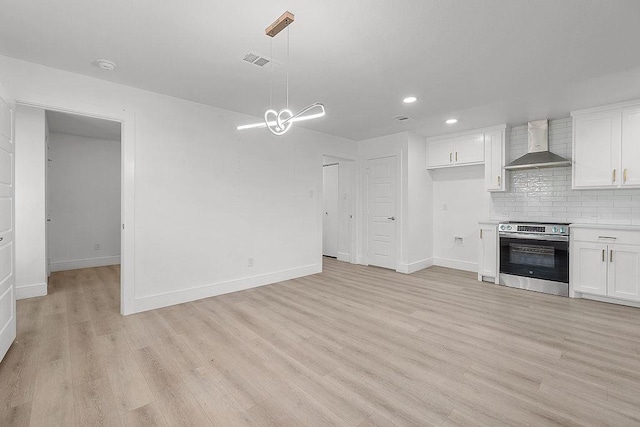 kitchen with wall chimney range hood, white cabinets, light wood finished floors, light countertops, and visible vents