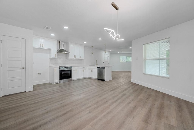 kitchen featuring wall chimney range hood, an inviting chandelier, stainless steel appliances, open floor plan, and visible vents