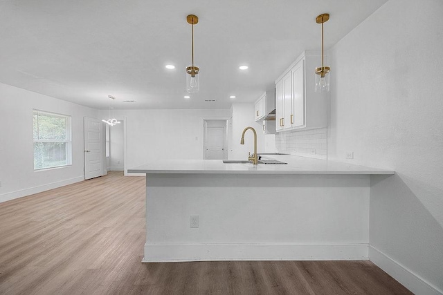 kitchen featuring a peninsula, baseboards, recessed lighting, white cabinets, and a sink