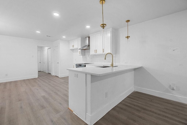 kitchen with baseboards, a sink, wall chimney exhaust hood, and wood finished floors
