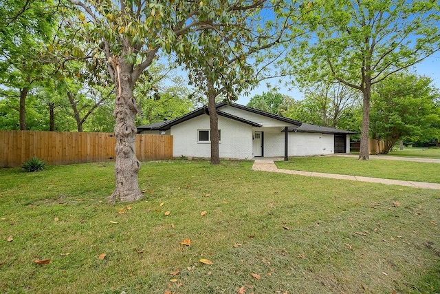 view of side of home featuring fence, an attached garage, a yard, and brick siding