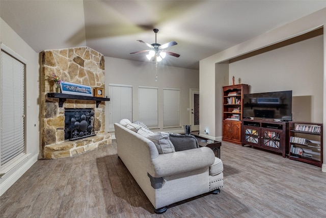living area featuring ceiling fan, lofted ceiling, a stone fireplace, and wood finished floors