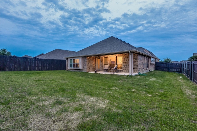 back of house with brick siding, a fenced backyard, a lawn, and a patio area