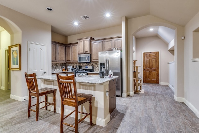 kitchen with visible vents, appliances with stainless steel finishes, tasteful backsplash, light stone countertops, and arched walkways