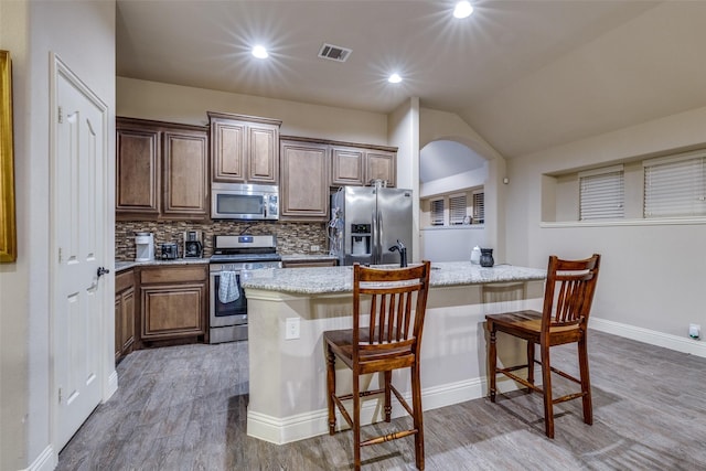 kitchen with light stone countertops, appliances with stainless steel finishes, a breakfast bar, wood finished floors, and tasteful backsplash