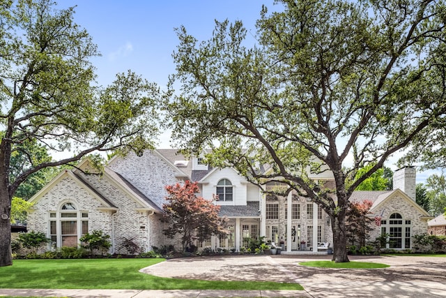 french country style house with brick siding, a chimney, and a front yard