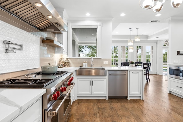 kitchen with appliances with stainless steel finishes, a sink, wall chimney exhaust hood, visible vents, and ornamental molding