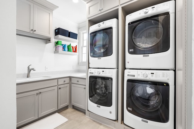washroom featuring cabinet space, stacked washer and dryer, a sink, light wood-type flooring, and ornamental molding
