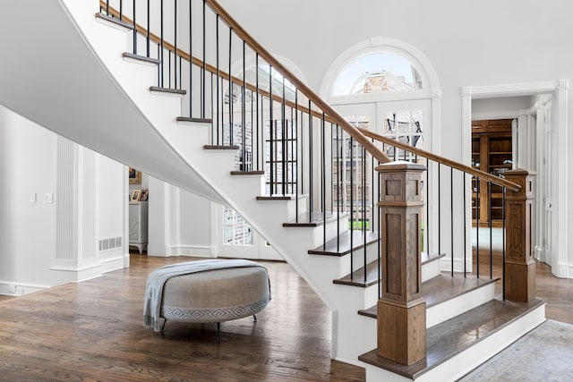 staircase featuring visible vents, a high ceiling, and wood finished floors