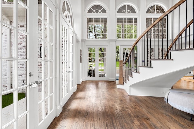 entrance foyer with french doors, stairs, a towering ceiling, and wood finished floors
