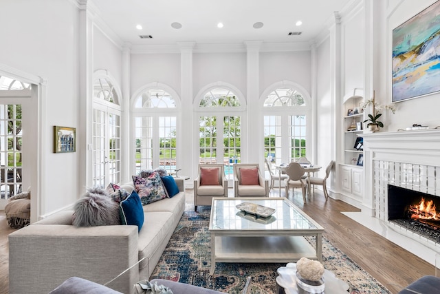 living area featuring a fireplace, french doors, wood finished floors, a towering ceiling, and visible vents