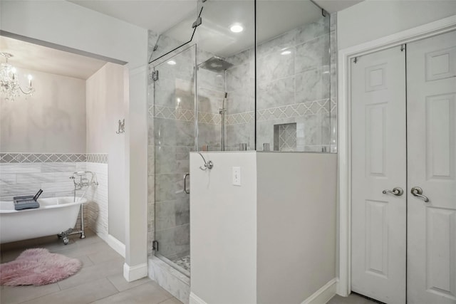 full bath with tile walls, tile patterned floors, a freestanding bath, a stall shower, and a notable chandelier