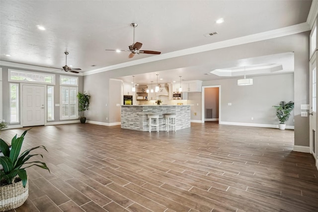 unfurnished living room with baseboards, crown molding, ceiling fan, and visible vents