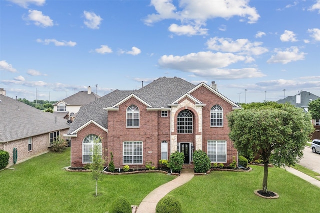 view of front of property with a shingled roof, a chimney, a front lawn, and brick siding