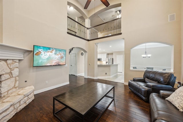 living room featuring a high ceiling, arched walkways, ceiling fan with notable chandelier, visible vents, and hardwood / wood-style flooring