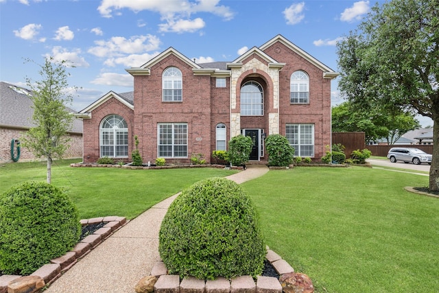 view of front facade with brick siding, fence, and a front yard