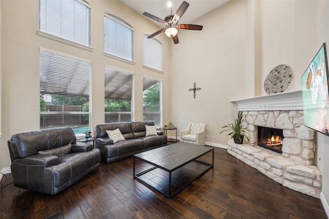living room featuring a ceiling fan, a towering ceiling, a fireplace, baseboards, and wood-type flooring