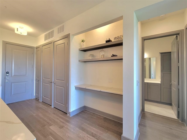 mudroom featuring built in desk, baseboards, visible vents, and wood finished floors