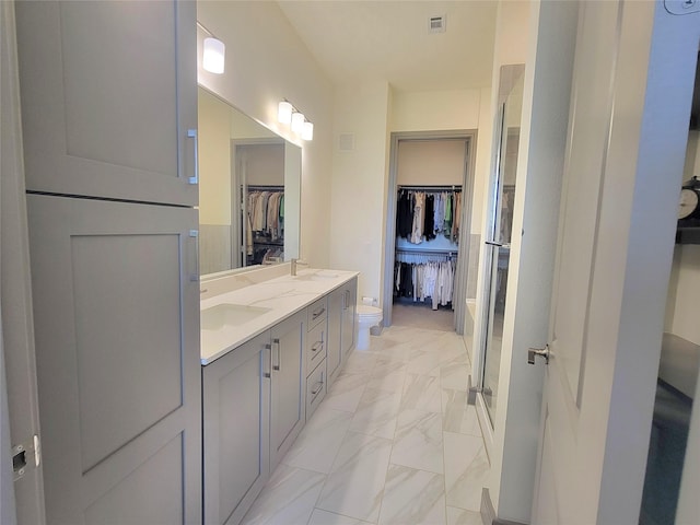 full bath with double vanity, toilet, marble finish floor, a spacious closet, and visible vents