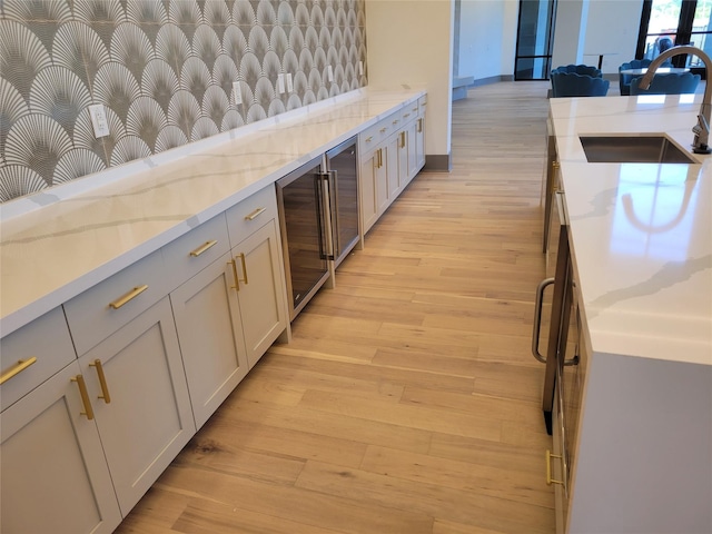 kitchen with beverage cooler, light stone counters, a sink, and light wood-style flooring