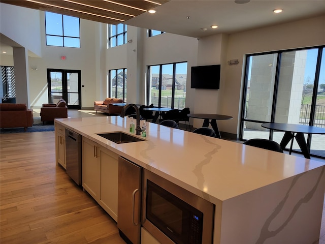 kitchen featuring stainless steel dishwasher, built in microwave, light wood-type flooring, a sink, and open floor plan